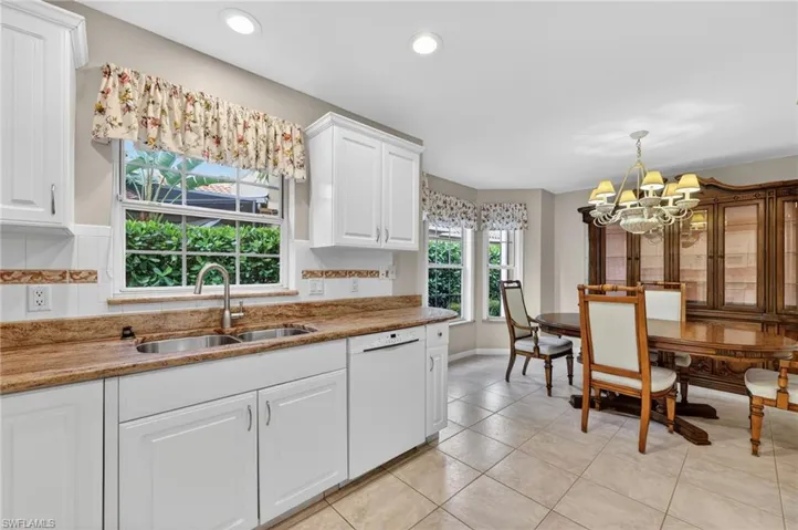 Kitchen with light stone countertops, white cabinets, dishwasher, suspended lighting, and light tile floors