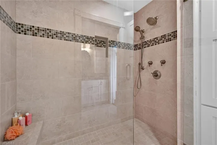 Walk-in shower featuring stone-finish wall tile, a glass enclosure, built-in bench seating, a recessed wall niche, and dual shower heads