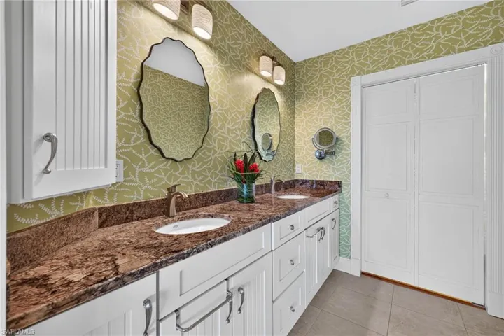 Dual-sink vanity with stone-finish countertop, white cabinetry, scalloped-edge mirrors, and wall-mounted light fixtures