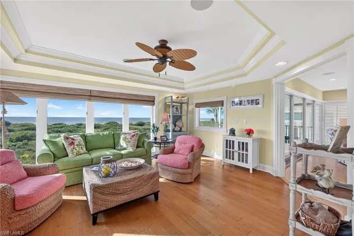 Tray ceiling, wood-finish flooring, recessed lighting, ceiling fan, and large windows with coastal scenery