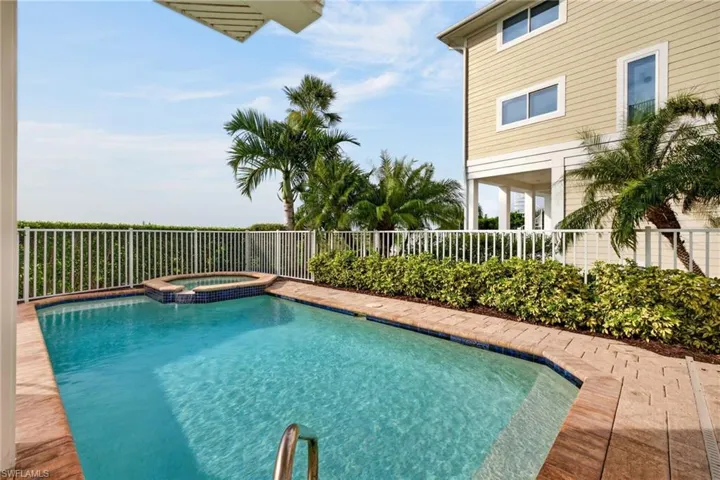 In-ground swimming pool with integrated spillover spa, paver surround, and perimeter white fencing