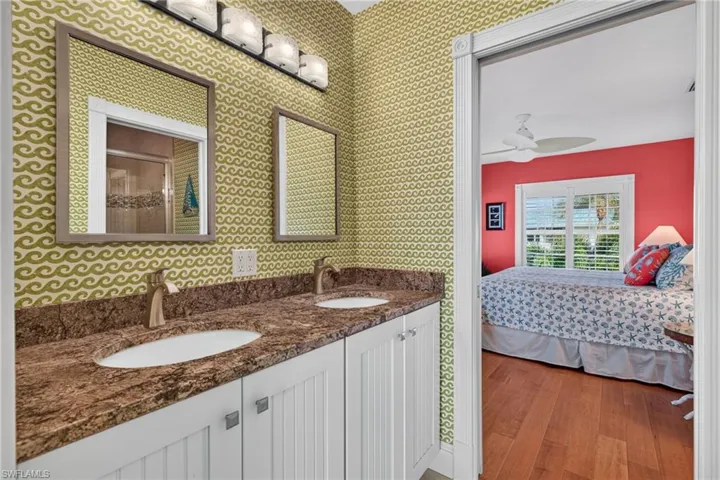 Double vanity featuring white beadboard cabinetry, stone-finish countertops, dual integrated sinks, and wall-mounted mirrors