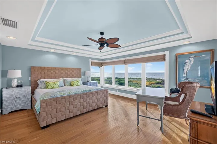 Tray ceiling with recessed lighting, wood-finish flooring, and expansive windows showcasing coastal scenery