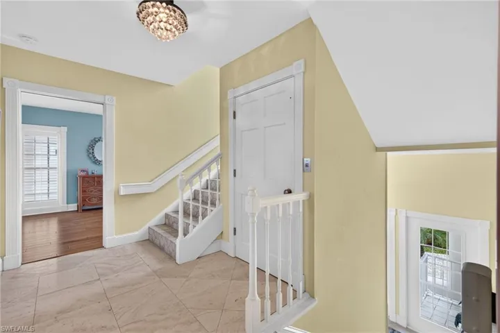 Foyer featuring large-format tile flooring, a multi-tiered crystal-style chandelier, a white six-panel interior door, and a white wooden staircase with decorative balusters