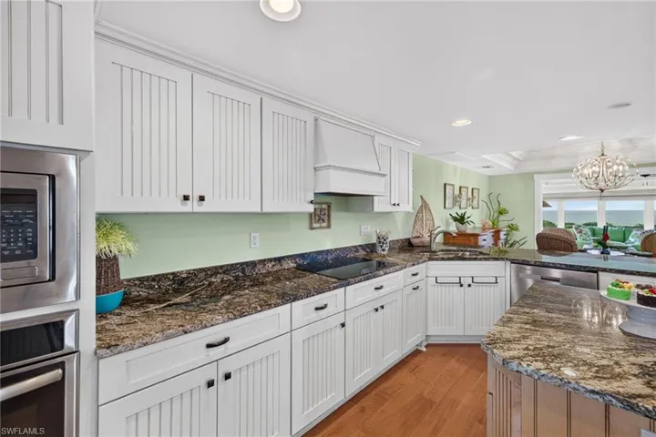 Kitchen featuring white beadboard cabinetry, stone countertops, integrated stainless steel appliances, a custom range hood, and wood-finish flooring