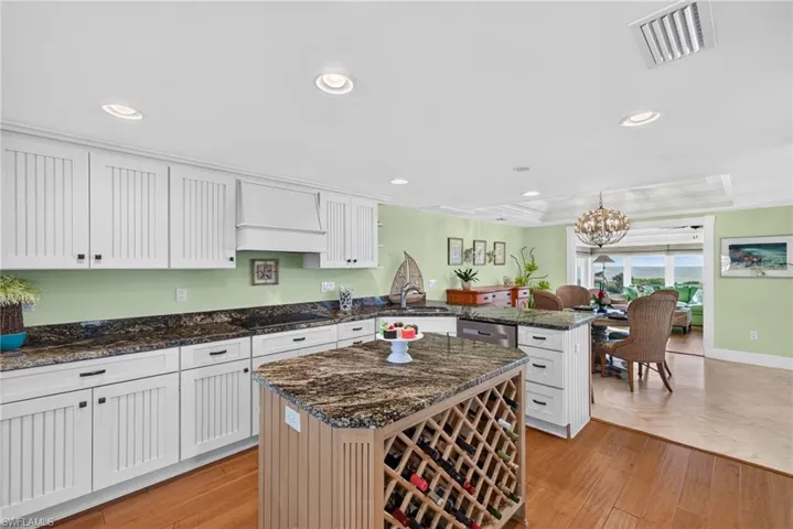 Kitchen featuring white beadboard cabinetry, stone countertops, a central island with built-in wine storage, recessed lighting, and wood-finish flooring