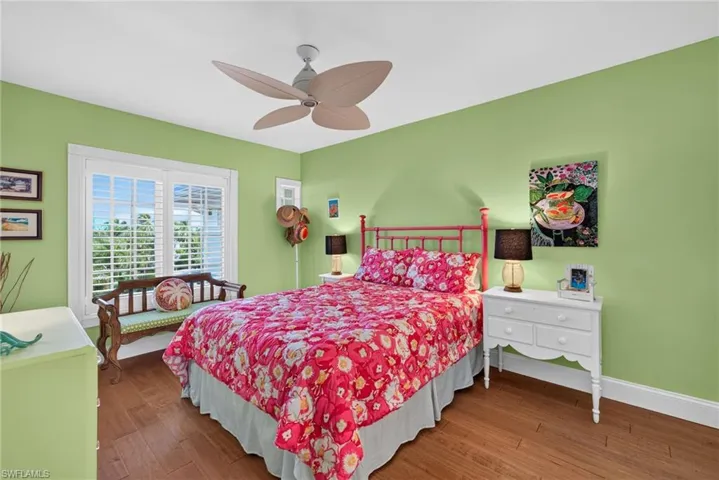 Room featuring wood-finish flooring, plantation shutters, and a multi-blade ceiling fan