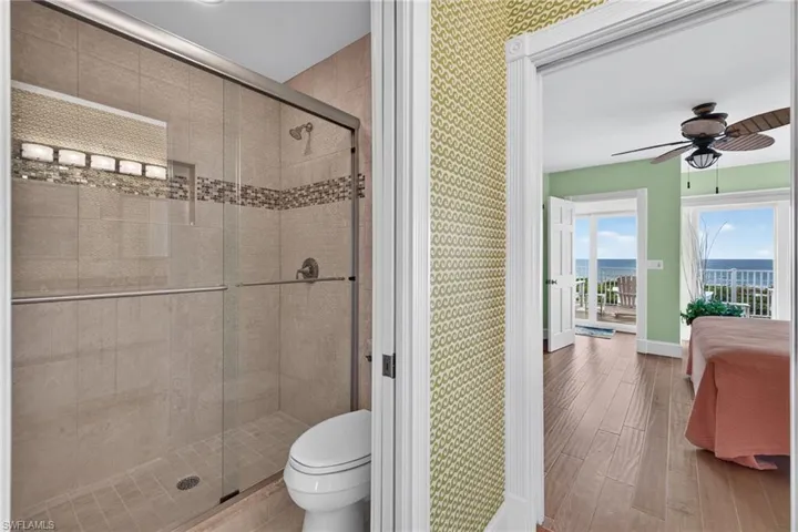 Walk-in shower with tile surround, decorative mosaic accent tile, and sliding glass enclosure, paired with wood-finish flooring and balcony access