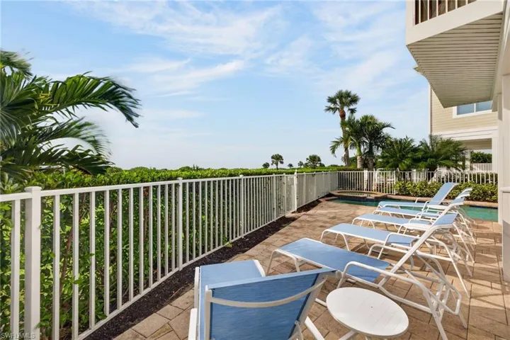 Paved patio area featuring an in-ground swimming pool, spa, white metal perimeter fencing, and established hedge landscaping