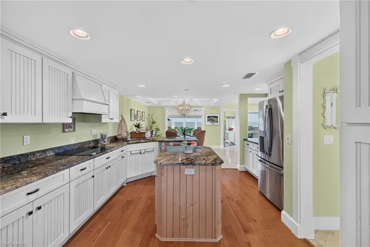 Kitchen featuring white beadboard cabinetry, stone-finish countertops, wood-finish flooring, a center island, and stainless steel appliances