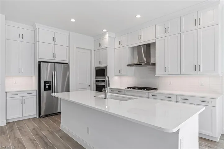 Kitchen featuring light wood-style flooring, wall chimney range hood, appliances with stainless steel finishes, and a sink