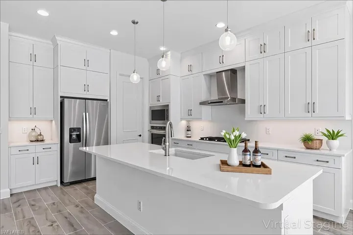 Kitchen with stainless steel appliances, light countertops, a sink, wall chimney exhaust hood, and white cabinetry