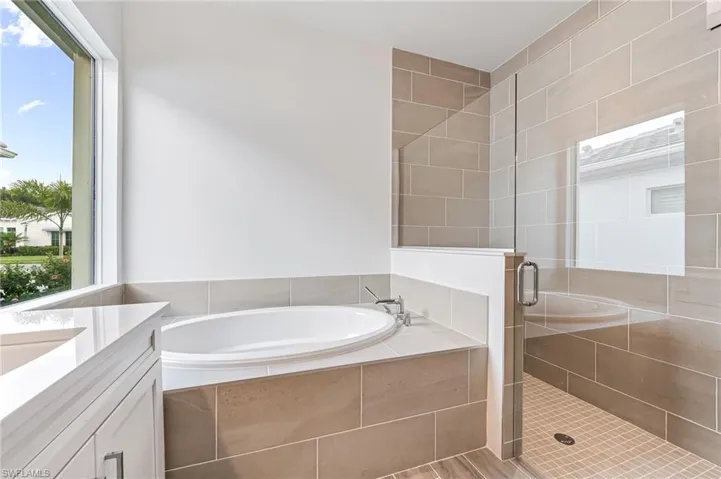 Bathroom with a bath, a healthy amount of sunlight, and a stall shower
