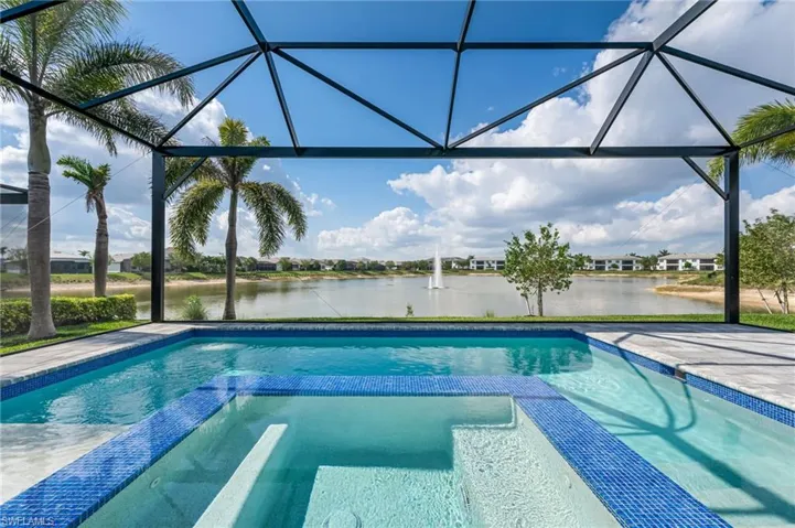 View of swimming pool featuring glass enclosure, a water view, and a pool with connected hot tub