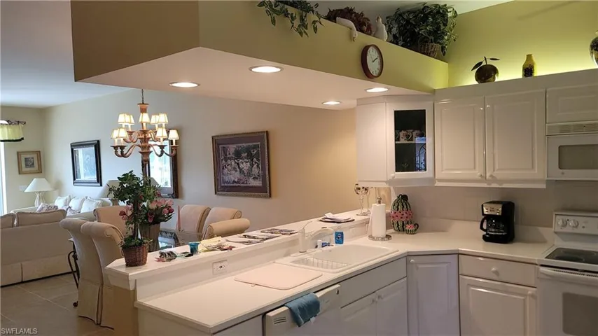 Kitchen with white appliances, a peninsula, backsplash, white cabinets, and a sink
