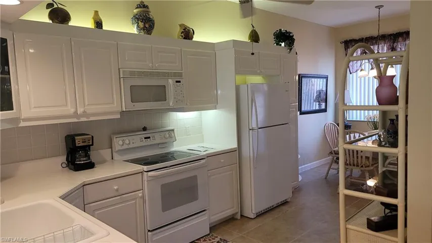 Kitchen featuring tasteful backsplash, light tile patterned floors, light countertops, white appliances, and white cabinetry