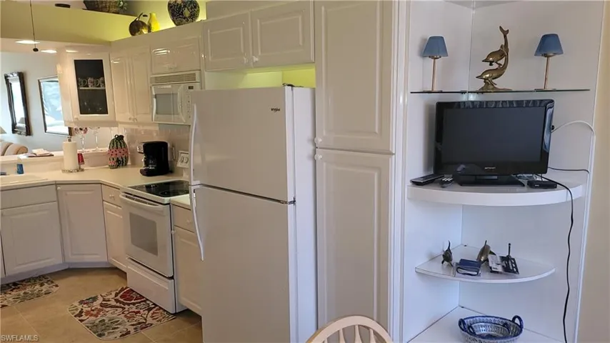 Kitchen featuring white appliances, glass insert cabinets, light countertops, white cabinetry, and backsplash