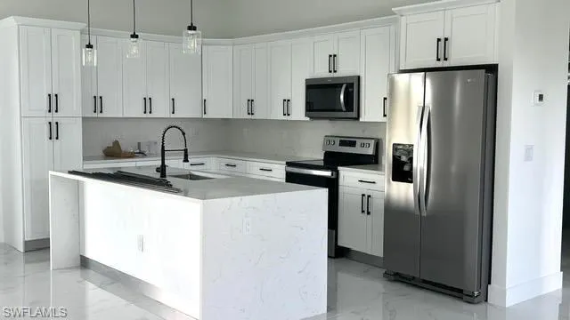 Kitchen with white cabinetry, stainless steel appliances, hanging light fixtures, sink, and a center island with sink