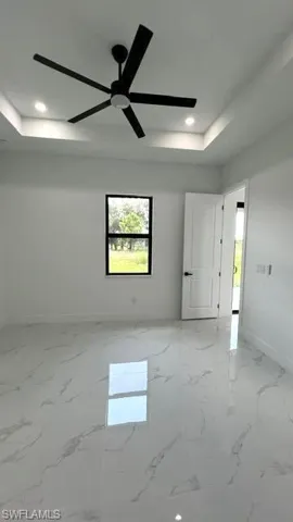 Empty room featuring light tile patterned flooring, ceiling fan, and a tray ceiling
