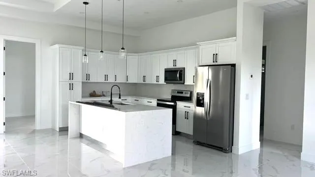 Kitchen featuring white cabinetry, an island with sink, appliances with stainless steel finishes, decorative light fixtures, and sink