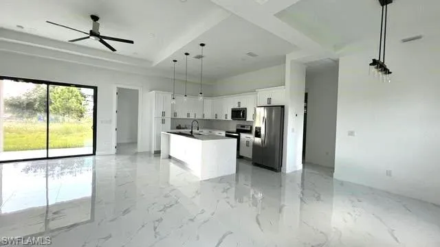 Kitchen with white cabinetry, light tile patterned floors, a kitchen island with sink, ceiling fan, and stainless steel appliances