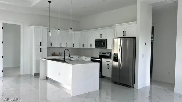Kitchen featuring appliances with stainless steel finishes, white cabinets, sink, pendant lighting, and an island with sink