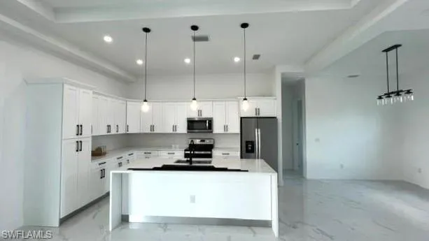 Kitchen with a center island, pendant lighting, stainless steel appliances, and white cabinetry