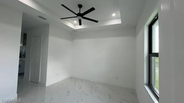 Unfurnished room with light tile patterned floors, ceiling fan, and a tray ceiling