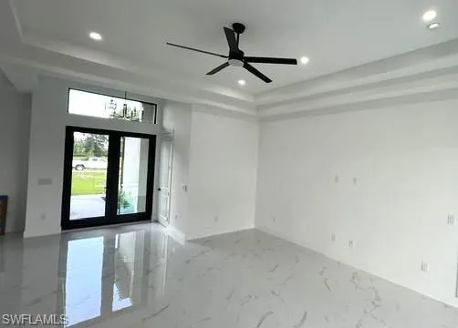 Unfurnished room with concrete flooring, ceiling fan, french doors, and a tray ceiling
