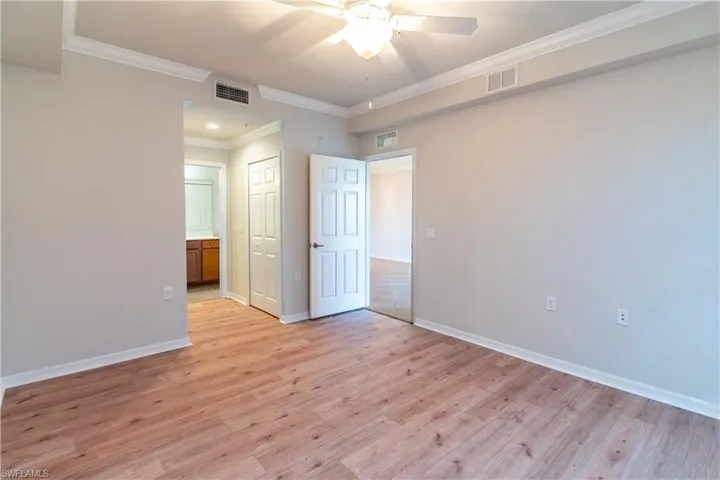 Unfurnished bedroom featuring ornamental molding, light wood-type flooring, a ceiling fan, a closet, and ensuite bath