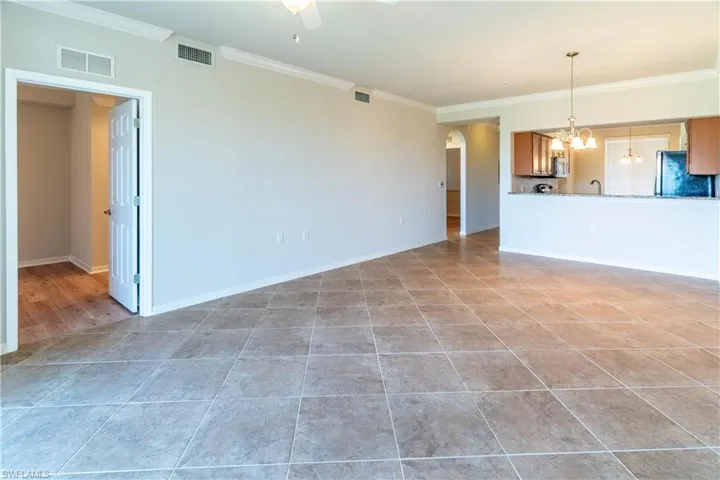 Unfurnished living room featuring crown molding, arched walkways, light tile patterned floors, ceiling fan, and a chandelier