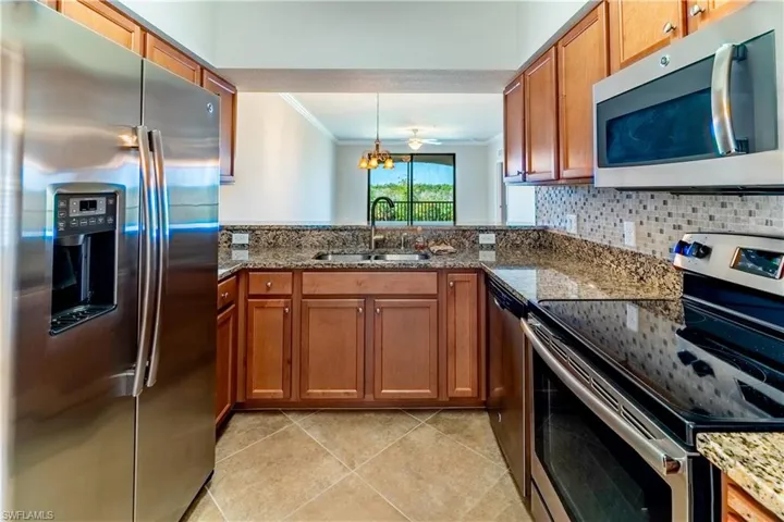 Kitchen with stainless steel appliances, ornamental molding, dark stone counters, brown cabinetry, and light tile patterned floors