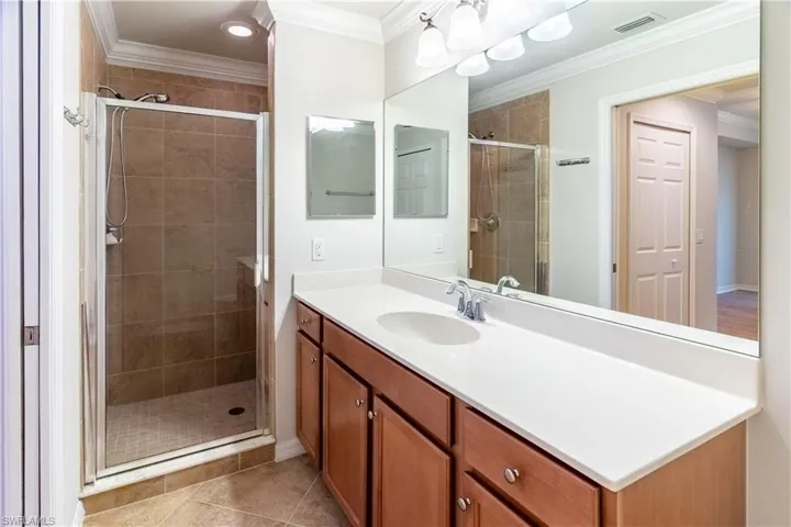 Bathroom featuring crown molding, a shower stall, vanity, and light tile patterned floors