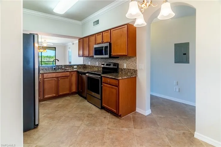 Kitchen featuring a chandelier, brown cabinets, appliances with stainless steel finishes, ornamental molding, and decorative backsplash