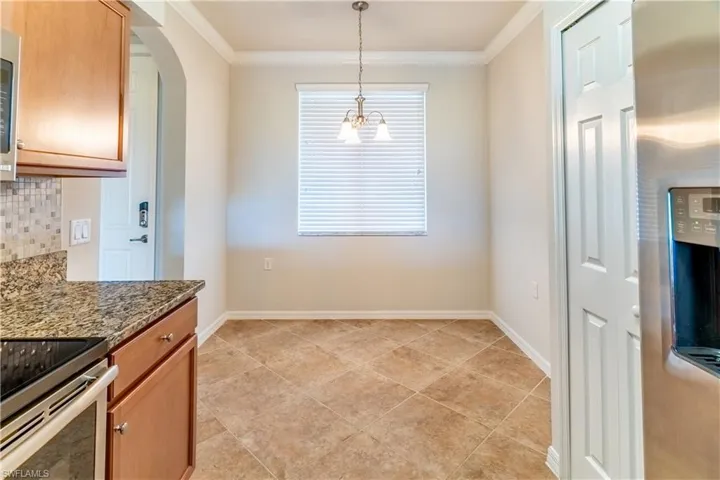 Kitchen with stainless steel appliances, dark stone counters, crown molding, hanging light fixtures, and arched walkways