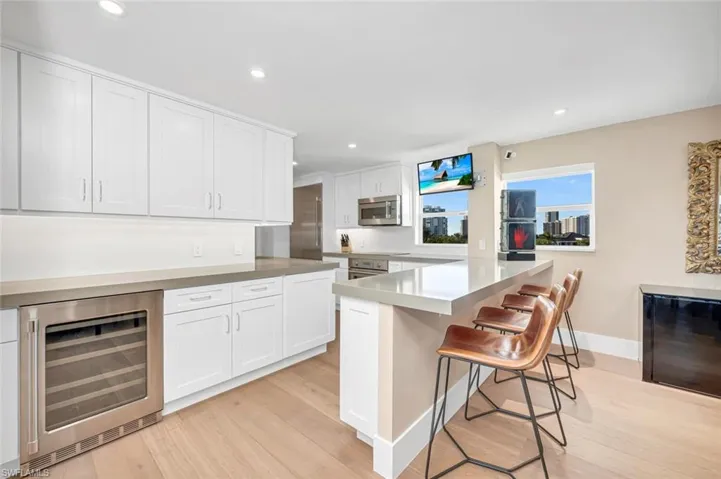 Kitchen with a kitchen bar, beverage cooler, light wood-style flooring, stainless steel appliances, and white cabinets