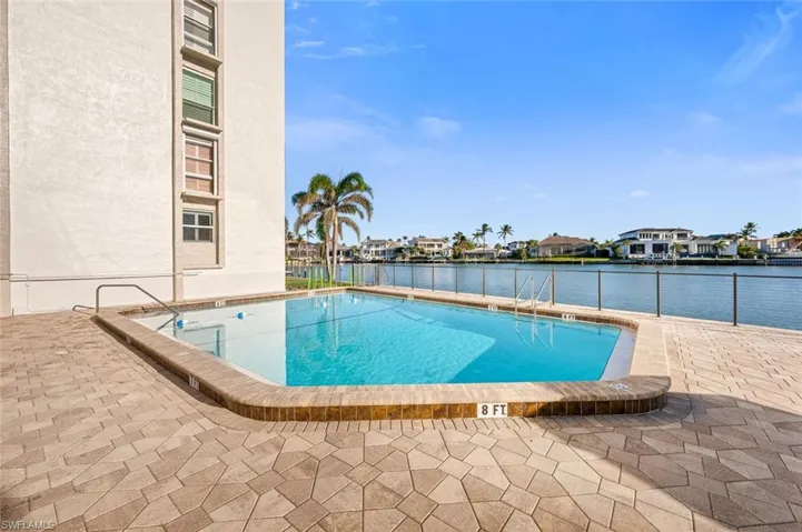 Community pool featuring fence, a water view, and a patio area