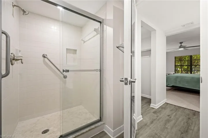 Ensuite bathroom featuring light wood finished floors, a shower stall, and a ceiling fan