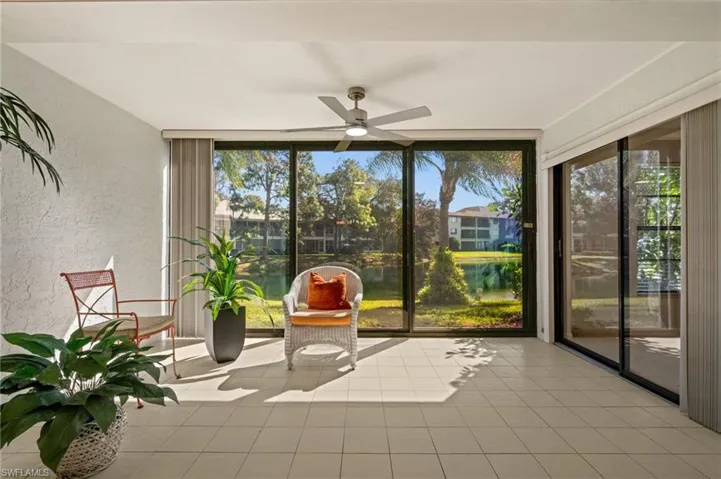 Unfurnished sunroom with ceiling fan, a textured wall, a water view, tile patterned floors, and expansive windows