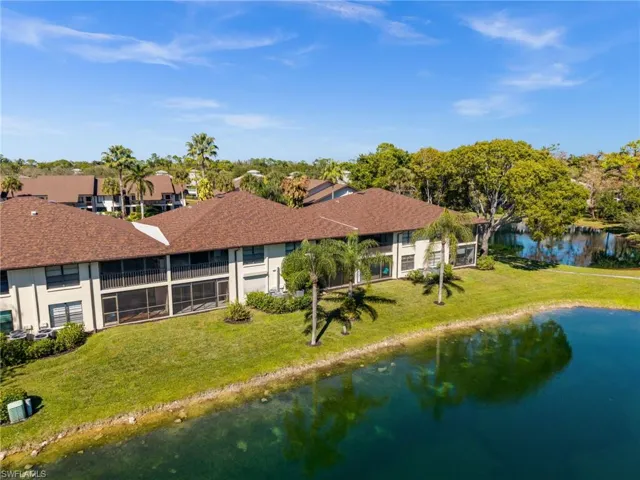 Back of property with a lawn, a shingled roof, a water view, and stucco siding