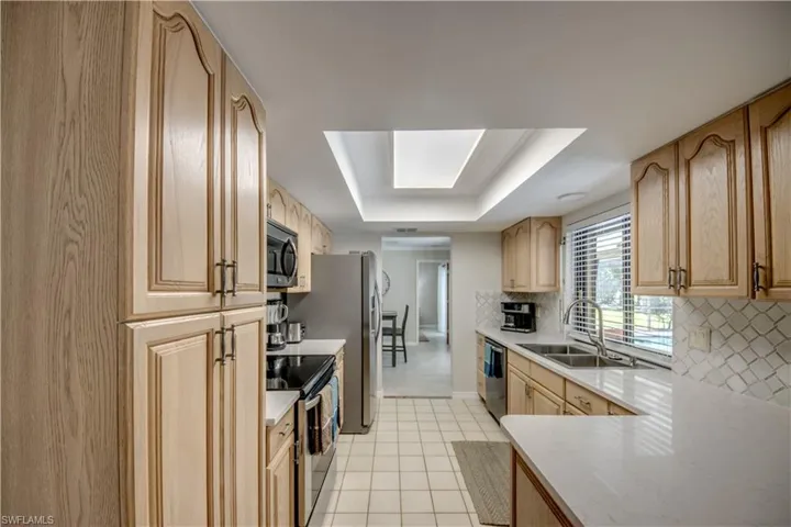 Kitchen with stainless steel appliances, a raised ceiling, backsplash, light tile floors, and sink