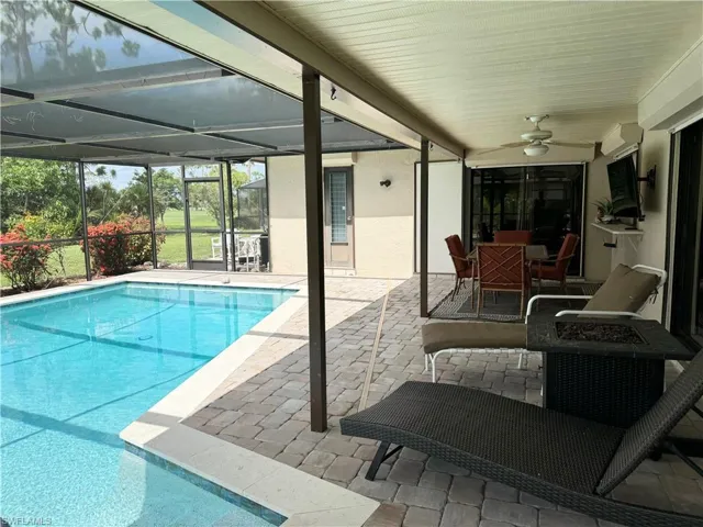 View of pool with glass enclosure, a patio area, and ceiling fan
