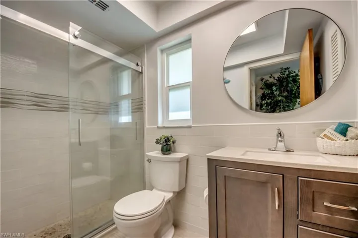 Bathroom featuring tile walls, backsplash, a shower with door, vanity, and toilet