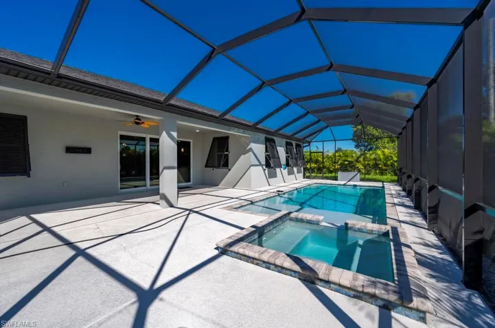 Screen-enclosed patio featuring a swimming pool, integrated spa with stone-style coping, expansive concrete deck, and a covered lanai with a ceiling fan