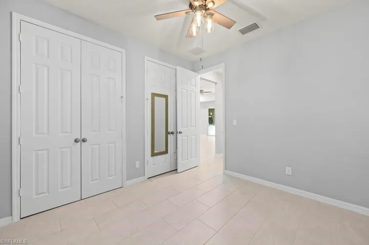 Room featuring light-toned tile flooring, neutral wall paint, multi-panel doors, and a ceiling fan with integrated lighting