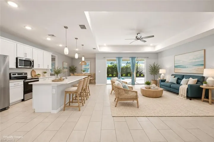 VIRTUALLY STAGED Open-concept floor plan featuring ceramic tile flooring, kitchen island with quartz countertops, recessed ceiling detail, and glass sliding doors