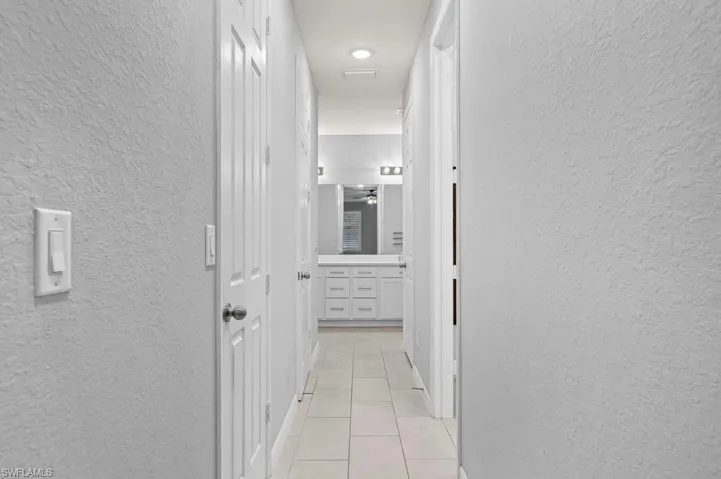 Hallway featuring light-toned tile flooring, textured wall finishes, and white-painted multi-panel doors with metallic hardware