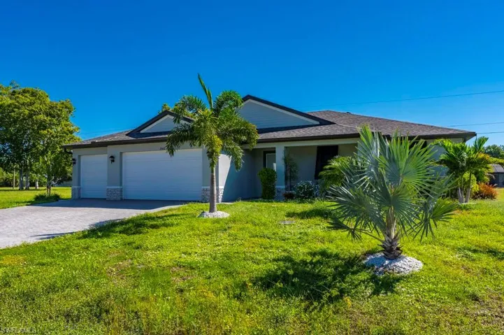 Single-story exterior featuring a hip roof, dual-bay garage, stone veneer accents, and paved driveway