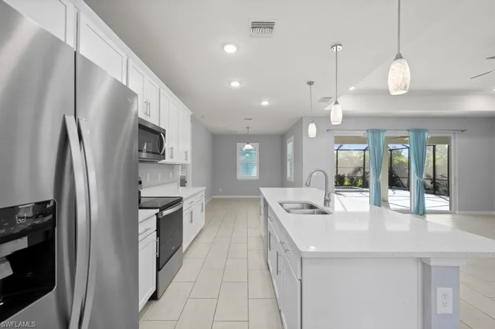 Kitchen featuring white shaker-style cabinetry, a quartz-topped center island with a dual-basin undermount sink, stainless steel appliances, recessed lighting, and tile flooring