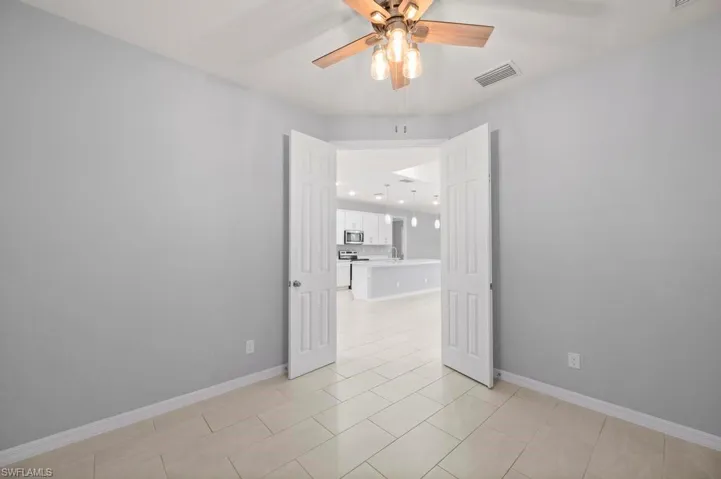 Interior room featuring dual paneled doors, neutral wall coloring, tile flooring, and a ceiling fan with multi-light fixture
